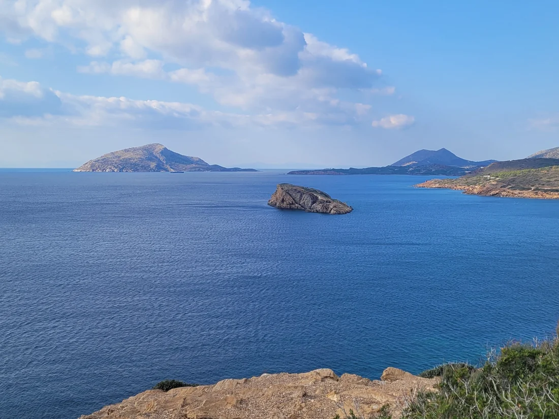 A rocky Greek coastline with a small island in a blue bay